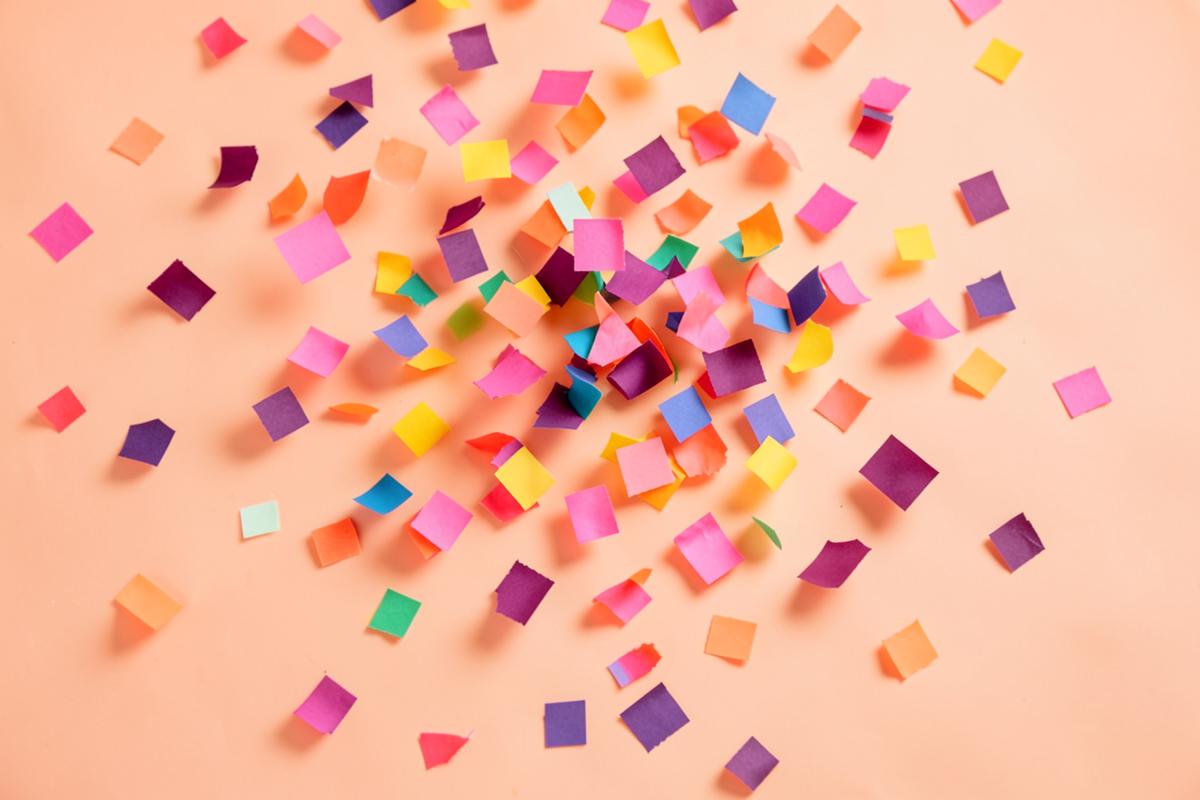 Colourful coral, pink and plum paper confetti scattered across a peach background